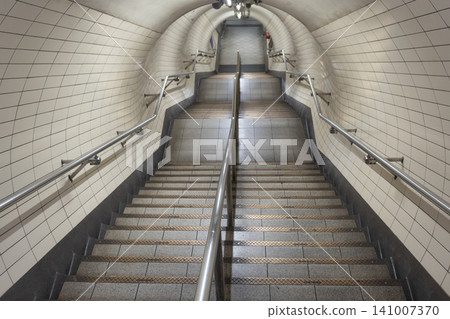Empty underground transit station staircase leading through a tiled pedestrian tunnel Empty underground transit station staircase leading through a tiled pedestrian tunnel 141007370