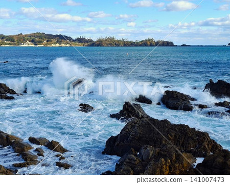 The rough waves crash violently against the rocky shores of Iwaizaki on the Sanriku coast, with Oshima Island visible in the distance—a truly breathtaking seascape. The rough waves crash violently against the rocky shores of Iwaizaki on the Sanriku coast, with Oshima Island visible in the distance—a truly breathtaking seascape. 141007473