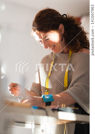Craftswoman sewing garment in bright fashion workshop 141007963