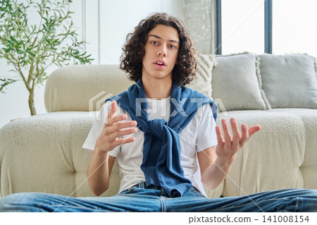 Curly teenage boy student talking and gesturing with hands during video call Curly teenage boy student talking and gesturing with hands during video call 141008154
