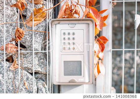 security keypad installed on outdoor wall with neutral mood and metal fence in the foreground, front view, for home automation systems, modern design, clean background. 141008368
