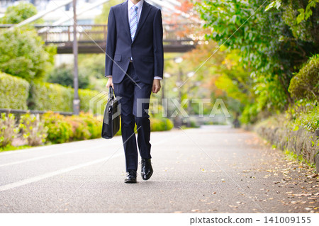 A businessman in his twenties walking outdoors A businessman in his twenties walking outdoors 141009155