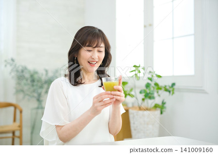 一位六十多歲的婦女在客廳喝蔬菜汁。 一位六十多歲的婦女在客廳喝蔬菜汁。 141009160