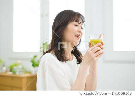 A woman in her 60s drinking vegetable juice in her living room. A woman in her 60s drinking vegetable juice in her living room. 141009163