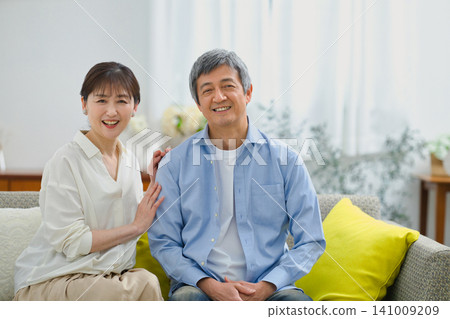 一對老年夫婦在沙發上放鬆,面帶微笑。 一對老年夫婦在沙發上放鬆,面帶微笑。 141009209