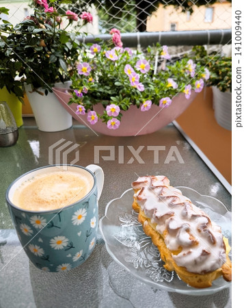 Coffee and an eclair on a balcony table with flowers. Coffee and an eclair on a balcony table with flowers. 141009440