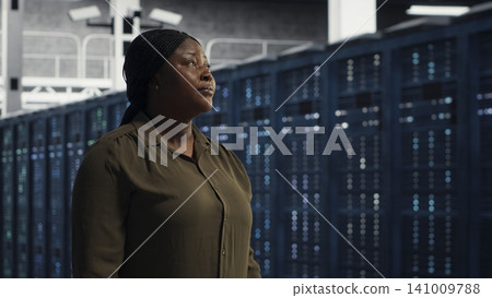 Data center administrator walks through a server room while overseeing IT infrastructure and network operations. Data center administrator walks through a server room while overseeing IT infrastructure and network operations. 141009788