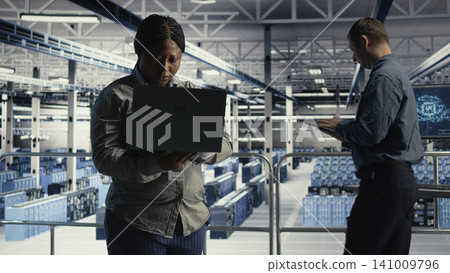Data center administrator uses a laptop to review an AI dashboard, working with AI technology and high performance systems. Data center administrator uses a laptop to review an AI dashboard, working with AI technology and high performance systems. 141009796