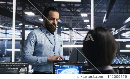 Data center manager oversees programmers reviewing AI diagnostics and machine learning systems. Data center manager oversees programmers reviewing AI diagnostics and machine learning systems. 141009856