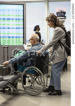 Senior man wheelchair user in airport terminal with woman assisting, holding boarding pass. Elderly travelers embracing disability-friendly tourism and equal opportunity, global travel. Senior man wheelchair user in airport terminal with woman assisting, holding boarding pass. Elderly travelers embracing disability-friendly tourism and equal opportunity, global travel. 141009860