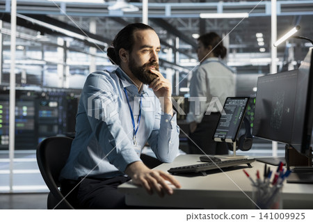 System administrator working with computer in server facility, managing server virtualization, running scripts. 141009925