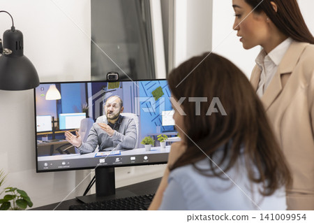 White businessman on device screen, having project discussion with female colleagues during virtual meeting. Diverse businesswomen listening to shareholder on video call, explain about company goals. White businessman on device screen, having project discussion with female colleagues during virtual meeting. Diverse businesswomen listening to shareholder on video call, explain about company goals. 141009954