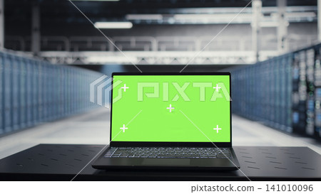 Data center technician uses a chroma key laptop to review server hardware stability and infrastructure maintenance. Data center technician uses a chroma key laptop to review server hardware stability and infrastructure maintenance. 141010096
