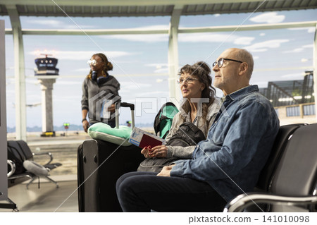 Smiling elderly man and woman sitting in airport lounge with luggage, having a chat and planning their trip while waiting for their plane. Retirees embracing freedom and bucket list travel goals. Smiling elderly man and woman sitting in airport lounge with luggage, having a chat and planning their trip while waiting for their plane. Retirees embracing freedom and bucket list travel goals. 141010098