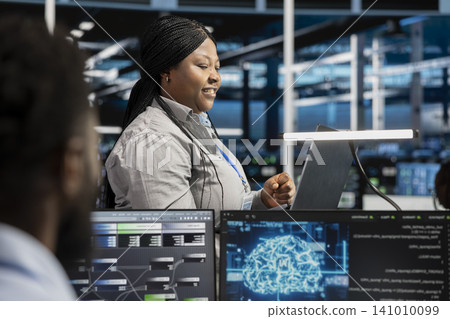Cheerful data center engineer applying AI to enhance operational efficiency and reduce downtime. Happy staff member designs and implements AI driven solutions for server facility equipment. Cheerful data center engineer applying AI to enhance operational efficiency and reduce downtime. Happy staff member designs and implements AI driven solutions for server facility equipment. 141010099
