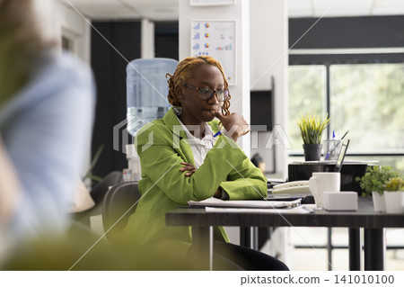 Corporate worker sitting deep in thought, considering creative ways to achieve company marketing targets. Pensive professional woman with finger on mouth, thinking on potential business projects. Corporate worker sitting deep in thought, considering creative ways to achieve company marketing targets. Pensive professional woman with finger on mouth, thinking on potential business projects. 141010100
