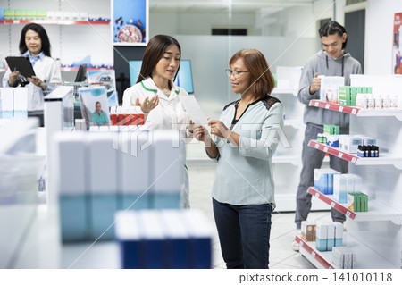 Professional pharmacist provides healthcare consultation while discussing medication packaging and treatment options with woman. Bright modern pharmacy reflects trust, expertise and patient care. Professional pharmacist provides healthcare consultation while discussing medication packaging and treatment options with woman. Bright modern pharmacy reflects trust, expertise and patient care. 141010118