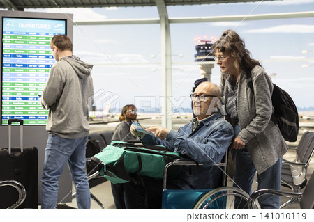 Senior man wheelchair user in airport terminal preparing for boarding with wife, travelers highlighting mobility aid and accessibility. Old couple enjoying leisure and world travel. Senior man wheelchair user in airport terminal preparing for boarding with wife, travelers highlighting mobility aid and accessibility. Old couple enjoying leisure and world travel. 141010119