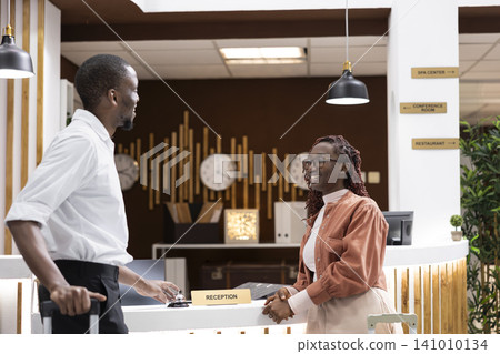 African american couple arriving at five star hotel front desk, waiting on hotel staff to help with booking confirmation and check-in process. Travelers on vacation at luxury resort. African american couple arriving at five star hotel front desk, waiting on hotel staff to help with booking confirmation and check-in process. Travelers on vacation at luxury resort. 141010134