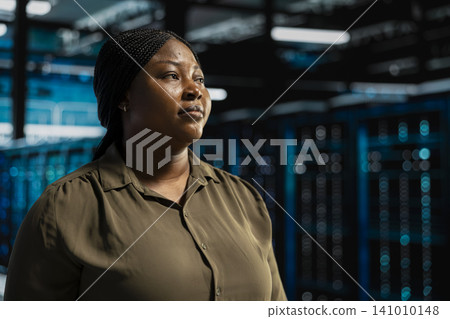 System admin walking in computing facility with server hardware supporting business needs, while doing checkup, ensuring equipment works at optimum operational performance for smooth operations. 141010148