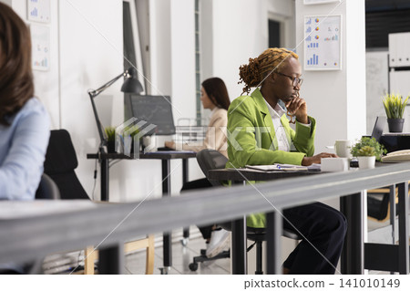 Skilled business advisor works at office desk, analyzing information on digital device and preparing reports. African american woman seated with focus, checking marketing strategy for presentations. Skilled business advisor works at office desk, analyzing information on digital device and preparing reports. African american woman seated with focus, checking marketing strategy for presentations. 141010149