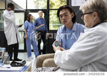 Doctor doing routine blood glucose test on patient in clinic waiting room, preparing for medical appointment. Healthcare worker uses digital glucometer to measure blood sugar levels in hospital lobby. 141010150