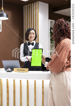 Vertical green screen tablet with asian staff and black guest at hotel reception, discussing about room reservation and payment at the front desk. Excellent customer service in tourism industry. Vertical green screen tablet with asian staff and black guest at hotel reception, discussing about room reservation and payment at the front desk. Excellent customer service in tourism industry. 141010151