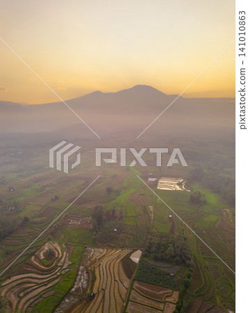 Beautiful panoramic aerial view of terraced rice fields at sunrise in Indonesia, surrounded by lush tropical greenery and palm trees. Beautiful panoramic aerial view of terraced rice fields at sunrise in Indonesia, surrounded by lush tropical greenery and palm trees. 141010863