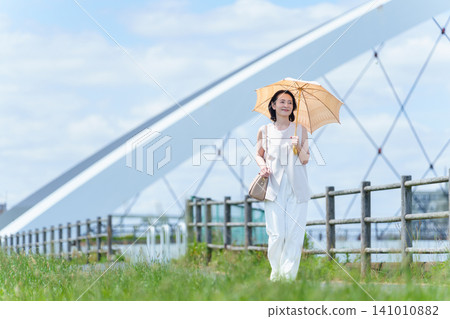 A woman walking along the riverbank with a parasol. A woman walking along the riverbank with a parasol. 141010882
