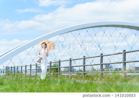 A woman walking along the riverbank with a parasol. A woman walking along the riverbank with a parasol. 141010883