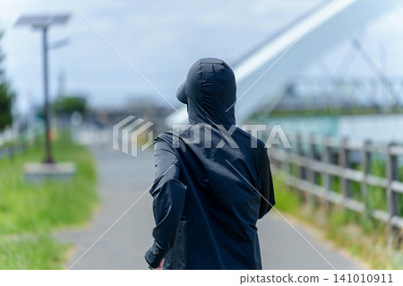 A woman's back view as she jogs, wearing a UV-cut hoodie. A woman's back view as she jogs, wearing a UV-cut hoodie. 141010911