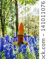 A wooden doll on a swing in a field of blue flowers 141011076