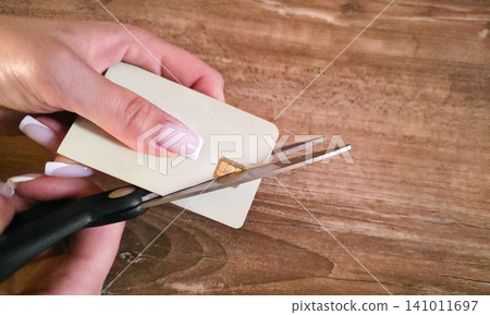 Macro shot of woman hands cutting a gold smart chip of a credit card with scissors. Wooden background, selective focus. Concept of card destruction, cyber security, final account closure, debt Macro shot of woman hands cutting a gold smart chip of a credit card with scissors. Wooden background, selective focus. Concept of card destruction, cyber security, final account closure, debt 141011697