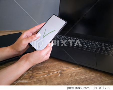 Close-up shot of female hands holding a mobile phone with a green checkmark icon displayed on the screen. Concept of successful online transaction, verified access, task completed, and safe Close-up shot of female hands holding a mobile phone with a green checkmark icon displayed on the screen. Concept of successful online transaction, verified access, task completed, and safe 141011700