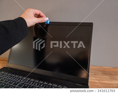 Close-up shot of a female hand placing a blue sticker cover over a laptop webcam. Concept of webcam hacking prevention, internet privacy, anti-spy protection, cybersecurity, and digital anxiety. Close-up shot of a female hand placing a blue sticker cover over a laptop webcam. Concept of webcam hacking prevention, internet privacy, anti-spy protection, cybersecurity, and digital anxiety. 141011703