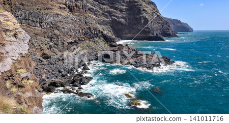 Rocky coastline with dark volcanic rocks and clear blue ocean waves lapping against the shore in a coastal landscape. High quality photo Rocky coastline with dark volcanic rocks and clear blue ocean waves lapping against the shore in a coastal landscape. High quality photo 141011716