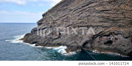 Rocky coastline with dark volcanic rocks and clear blue ocean waves lapping against the shore in a coastal landscape. High quality photo Rocky coastline with dark volcanic rocks and clear blue ocean waves lapping against the shore in a coastal landscape. High quality photo 141011724