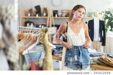 Young woman choosing denim shorts in clothing store Young woman choosing denim shorts in clothing store 141012039