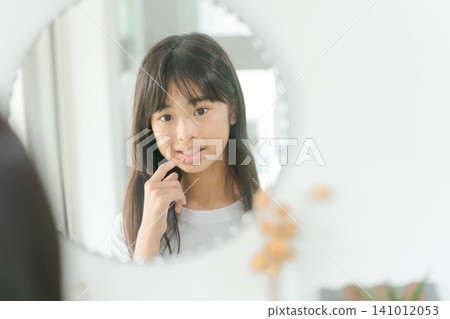 Elementary school girl looking at her mouth in the mirror Elementary school girl looking at her mouth in the mirror 141012053