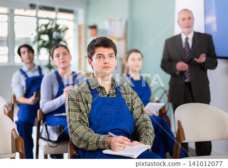 Young male student worker listening to lecture with teacher in background 141012077