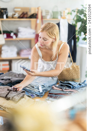 Young woman with phone in her hands scanning clothing labels Young woman with phone in her hands scanning clothing labels 141012094