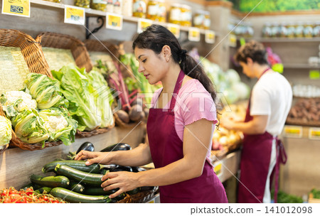 Woman worker seller in grocery vegetable shop and zucchini Woman worker seller in grocery vegetable shop and zucchini 141012098