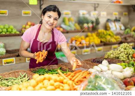 Female salesperson places fresh carrots on supermarket counter. Female salesperson places fresh carrots on supermarket counter. 141012101