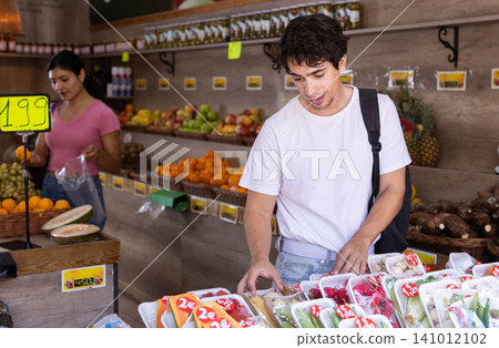 Male customer choosing vegetables and fruits in packaging at grocery store Male customer choosing vegetables and fruits in packaging at grocery store 141012102