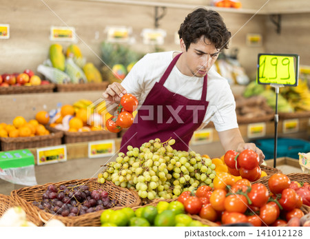 Male seller wearing apron holding tomatoes in hand in grocery shop Male seller wearing apron holding tomatoes in hand in grocery shop 141012128