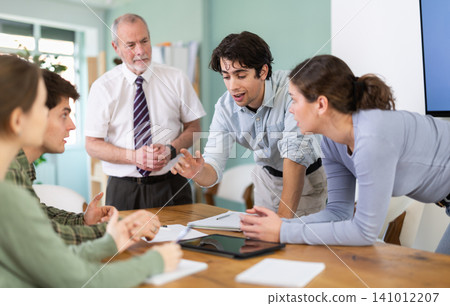 Young students discussing a topic around table monitored by senior teacher Young students discussing a topic around table monitored by senior teacher 141012207