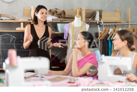 Young female teacher speaking students during dressmaking class Young female teacher speaking students during dressmaking class 141012208