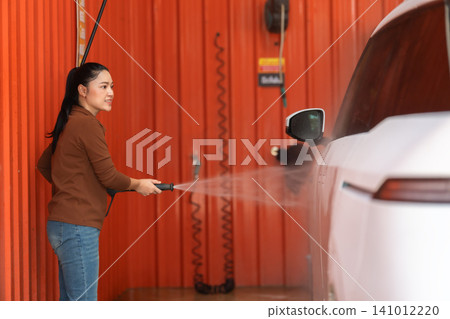 woman washing car with water hose in a self-service car wash station woman washing car with water hose in a self-service car wash station 141012220