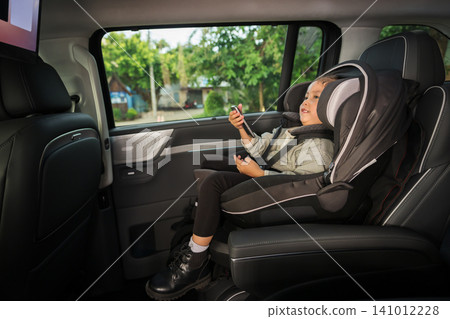 preschool child girl watching rear entertainment screen or ceiling screen while sitting in car seat, safety baby chair travelling preschool child girl watching rear entertainment screen or ceiling screen while sitting in car seat, safety baby chair travelling 141012228