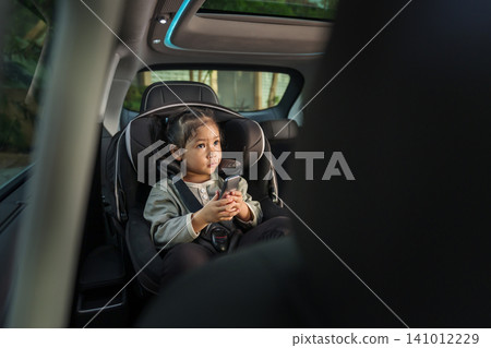 preschool child girl watching rear entertainment screen or ceiling screen while sitting in car seat, safety baby chair travelling preschool child girl watching rear entertainment screen or ceiling screen while sitting in car seat, safety baby chair travelling 141012229